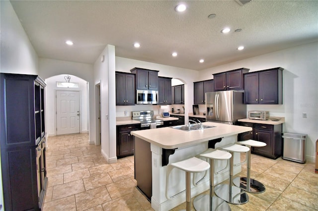 kitchen with dark brown cabinetry, sink, a center island with sink, a kitchen breakfast bar, and stainless steel appliances