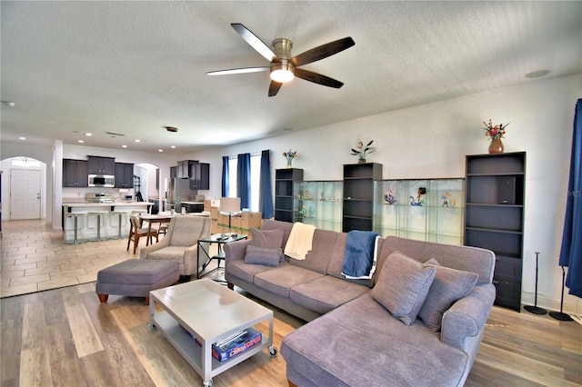 living room featuring ceiling fan, light hardwood / wood-style floors, and a textured ceiling