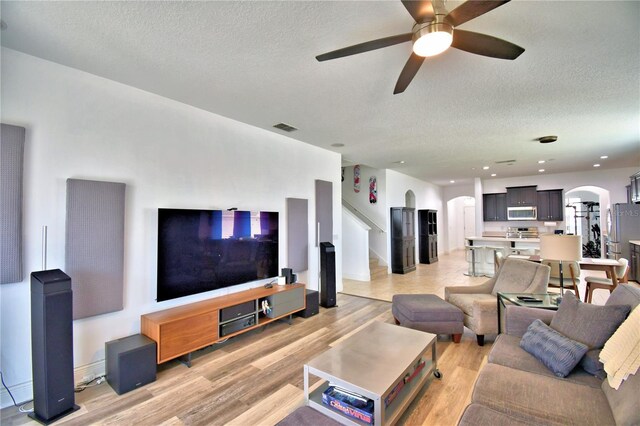 living room featuring ceiling fan, a textured ceiling, and light wood-type flooring