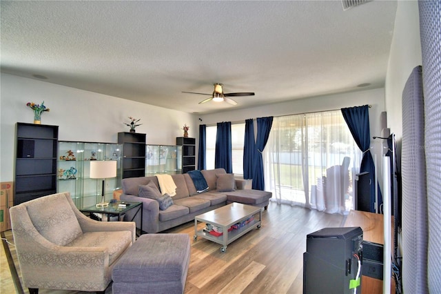 living room featuring ceiling fan, a textured ceiling, and light wood-type flooring