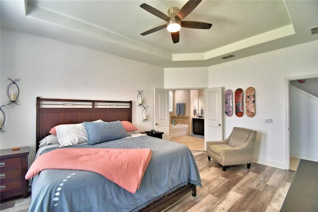 bedroom with ensuite bathroom, hardwood / wood-style floors, ceiling fan, a tray ceiling, and a textured ceiling