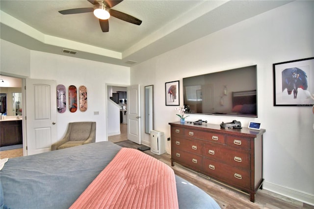 bedroom with ceiling fan, a raised ceiling, and light hardwood / wood-style flooring