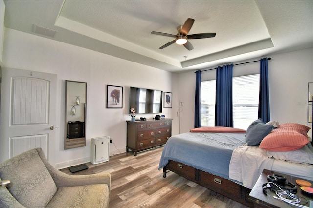 bedroom with a tray ceiling, light hardwood / wood-style floors, and ceiling fan