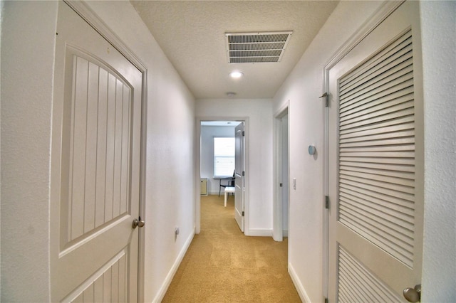 hallway featuring light colored carpet and a textured ceiling