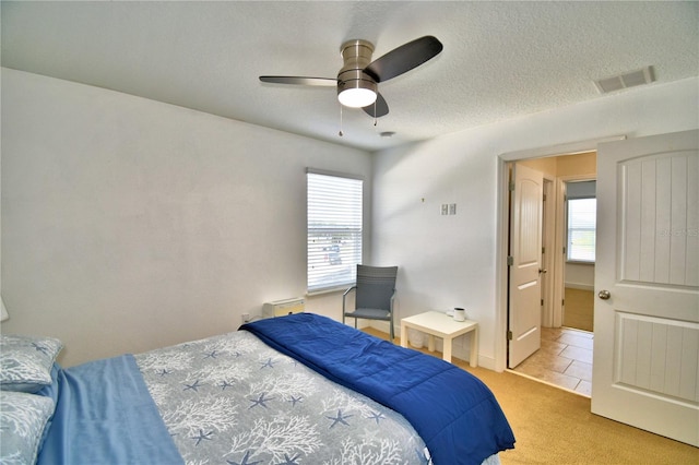 bedroom with ceiling fan, light colored carpet, and a textured ceiling