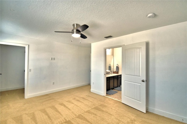 unfurnished bedroom featuring ensuite bath, a spacious closet, ceiling fan, light carpet, and a textured ceiling