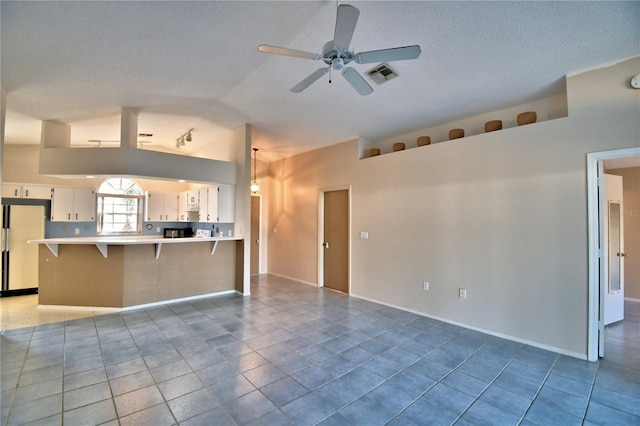 unfurnished living room with ceiling fan, lofted ceiling, a textured ceiling, and light tile patterned floors