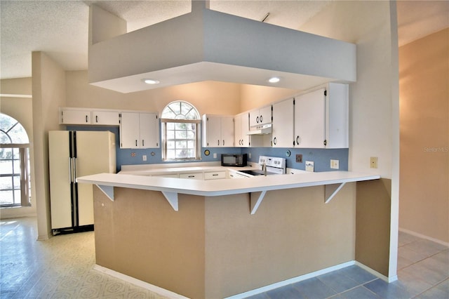 kitchen featuring white appliances, a kitchen breakfast bar, white cabinets, vaulted ceiling, and kitchen peninsula