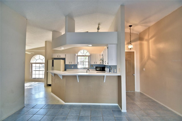 kitchen featuring lofted ceiling, white cabinetry, hanging light fixtures, kitchen peninsula, and white fridge