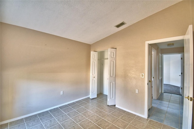 unfurnished bedroom with lofted ceiling, a textured ceiling, a closet, and light tile patterned floors