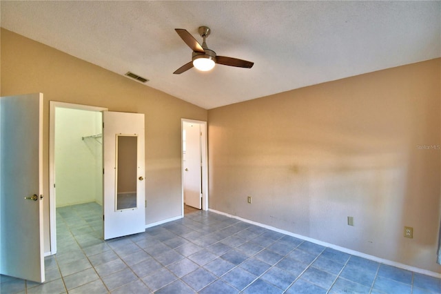 unfurnished bedroom featuring ceiling fan, a spacious closet, vaulted ceiling, tile patterned floors, and a closet