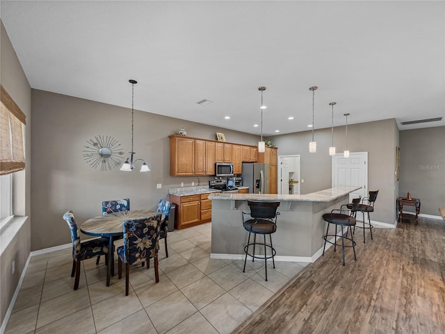 kitchen featuring light hardwood / wood-style flooring, a breakfast bar, appliances with stainless steel finishes, a center island, and decorative light fixtures