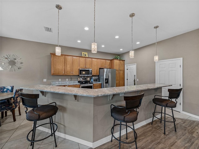 kitchen with light stone counters, decorative light fixtures, a kitchen breakfast bar, stainless steel appliances, and a large island