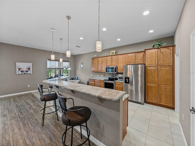 kitchen with appliances with stainless steel finishes, pendant lighting, a kitchen bar, a large island with sink, and light stone countertops