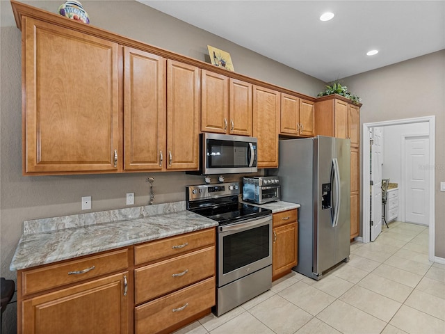 kitchen with stainless steel appliances, light stone countertops, and light tile patterned floors