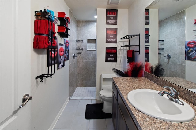 bathroom with tile patterned flooring, vanity, a tile shower, and toilet