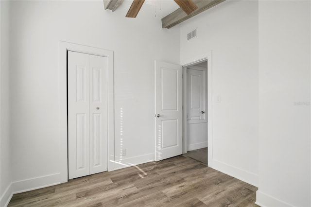 unfurnished bedroom with ceiling fan, light wood-type flooring, beam ceiling, and a closet