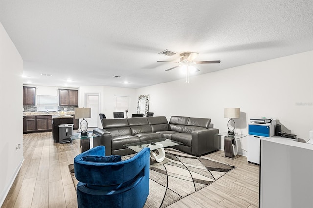 living room featuring a textured ceiling, light wood finished floors, visible vents, and a ceiling fan