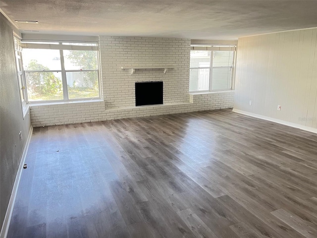 unfurnished living room with brick wall, a textured ceiling, dark hardwood / wood-style flooring, and a fireplace