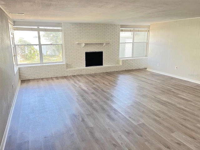 unfurnished living room with a textured ceiling, a fireplace, brick wall, and wood-type flooring