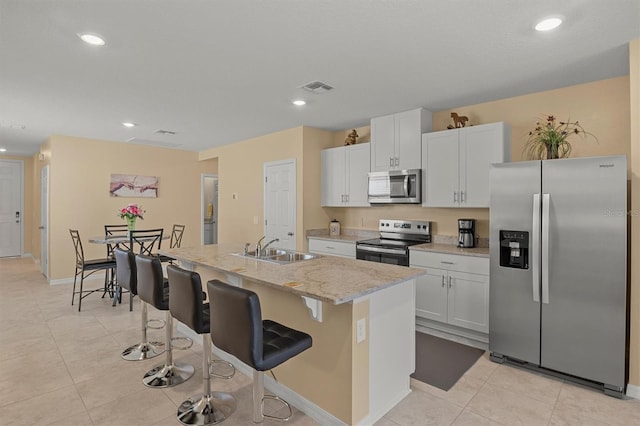 kitchen with an island with sink, white cabinetry, sink, stainless steel appliances, and light stone countertops