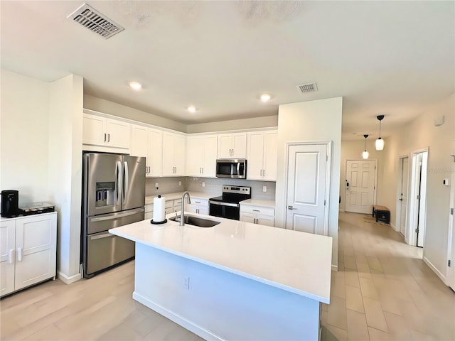 kitchen featuring sink, appliances with stainless steel finishes, an island with sink, white cabinets, and decorative light fixtures