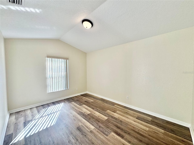 unfurnished room with hardwood / wood-style floors, vaulted ceiling, and a textured ceiling