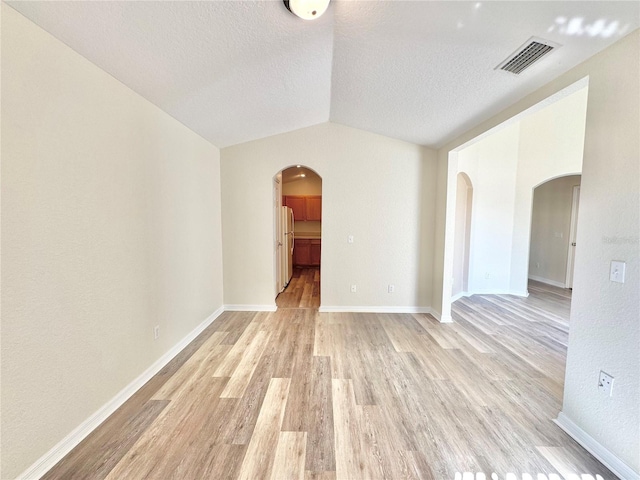 empty room featuring lofted ceiling, a textured ceiling, and light wood-type flooring