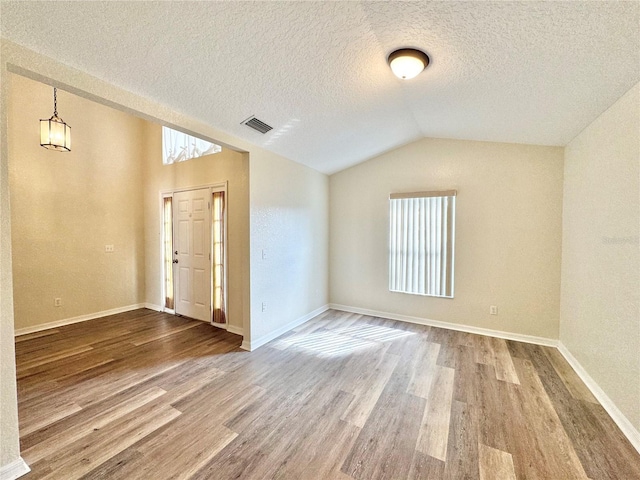 empty room featuring vaulted ceiling, hardwood / wood-style floors, and a textured ceiling