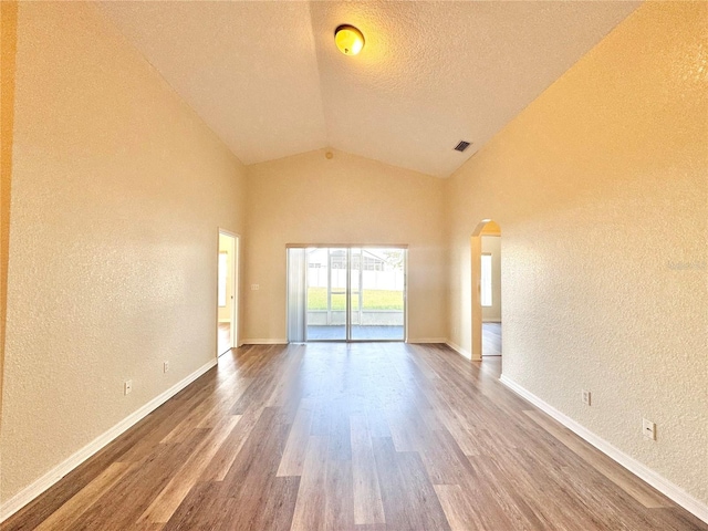 unfurnished room with lofted ceiling, wood-type flooring, and a textured ceiling