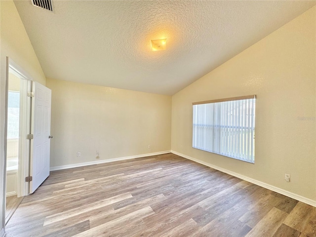 empty room featuring a wealth of natural light, vaulted ceiling, a textured ceiling, and light wood-type flooring