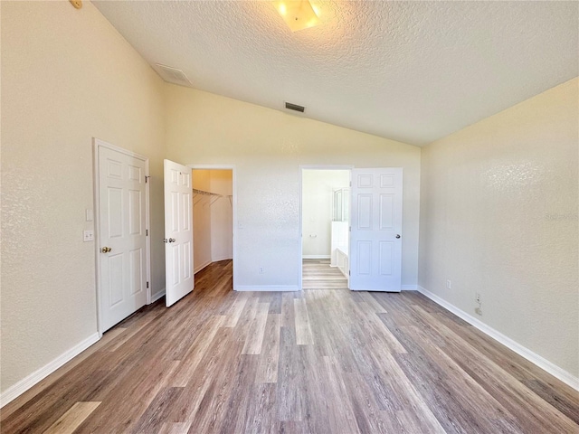 unfurnished bedroom with lofted ceiling, ensuite bath, light hardwood / wood-style flooring, a textured ceiling, and a spacious closet