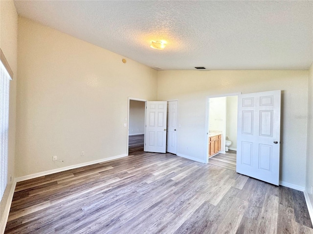 unfurnished bedroom featuring ensuite bath, lofted ceiling, a textured ceiling, and light wood-type flooring