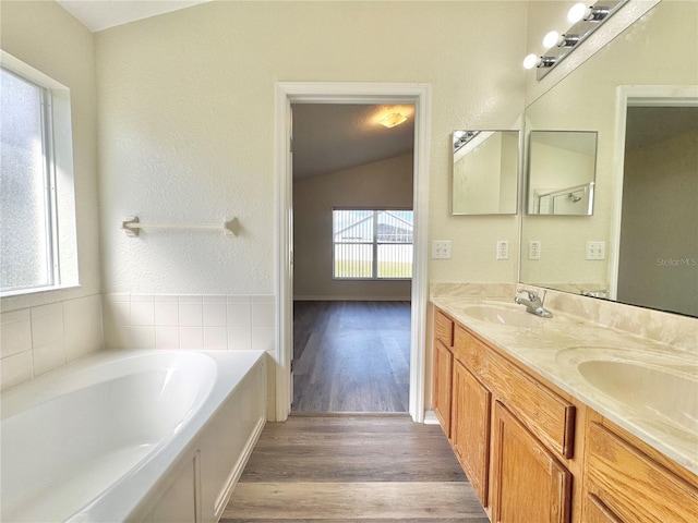 bathroom with a washtub, hardwood / wood-style floors, vanity, and vaulted ceiling