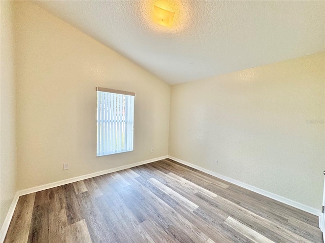 empty room featuring lofted ceiling, hardwood / wood-style floors, and a textured ceiling