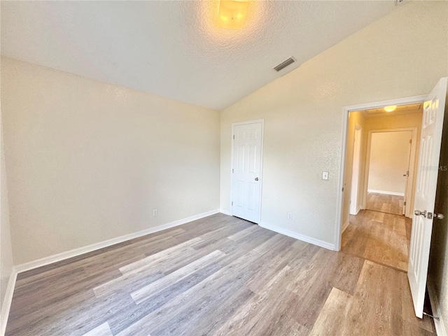 unfurnished bedroom with vaulted ceiling, light hardwood / wood-style flooring, and a textured ceiling