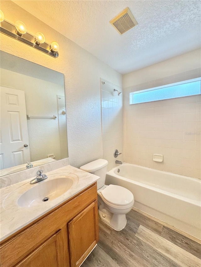 full bathroom with toilet, tiled shower / bath, a textured ceiling, vanity, and hardwood / wood-style floors