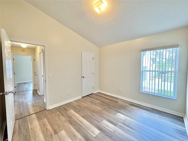 unfurnished bedroom with light hardwood / wood-style flooring, vaulted ceiling, and a textured ceiling