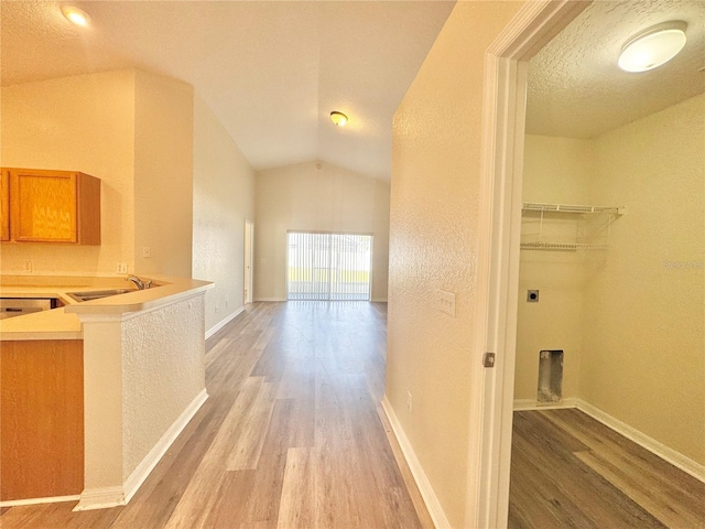 hall featuring vaulted ceiling, sink, light hardwood / wood-style flooring, and a textured ceiling