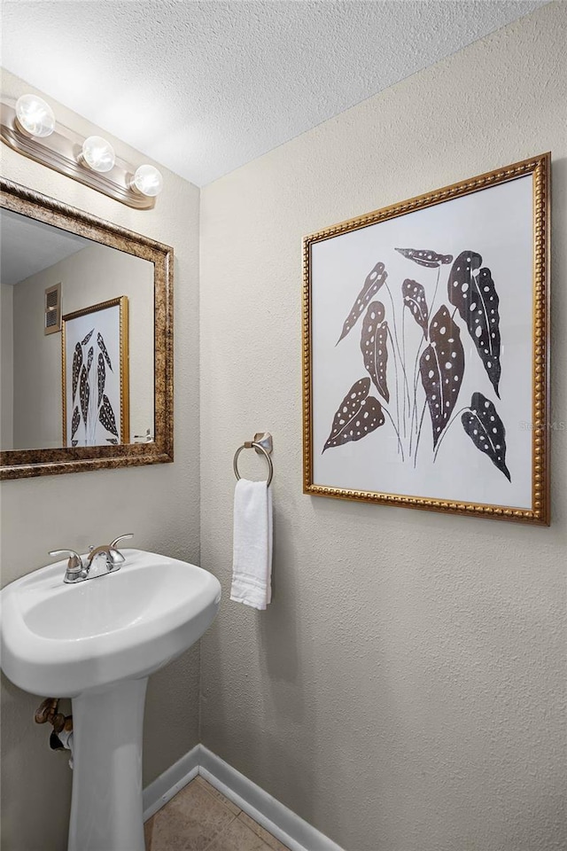 bathroom featuring baseboards, a sink, a textured wall, and a textured ceiling