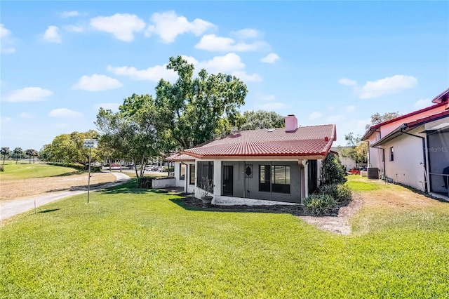 back of property with a chimney, a tile roof, stucco siding, central AC, and a lawn