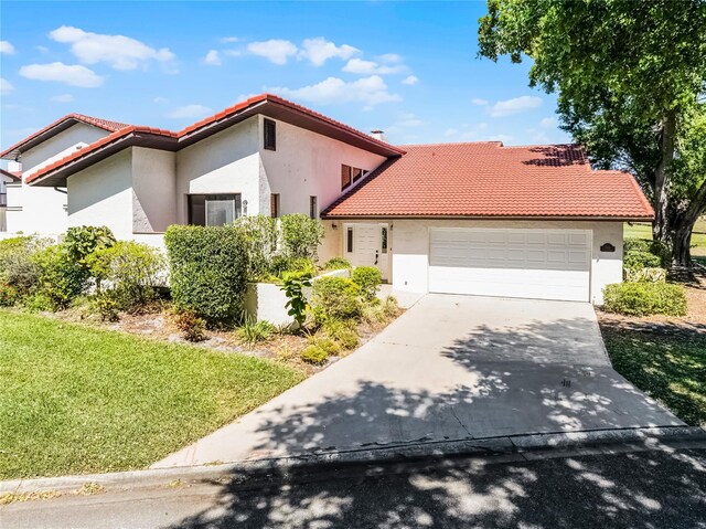 mediterranean / spanish-style house with a tile roof, stucco siding, an attached garage, driveway, and a front lawn