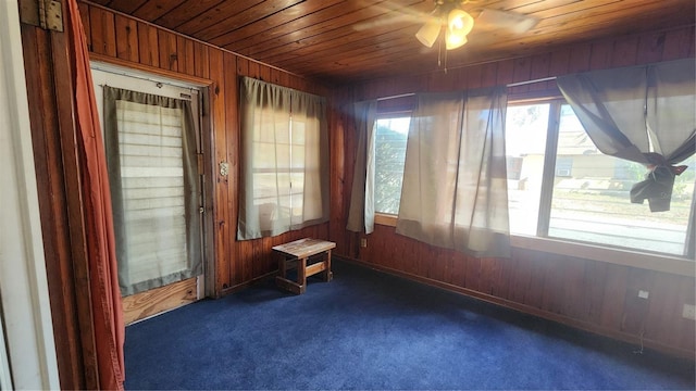 carpeted spare room with wood ceiling, ceiling fan, and wood walls