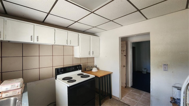 kitchen with a paneled ceiling, white cabinetry, decorative backsplash, light tile patterned floors, and electric range