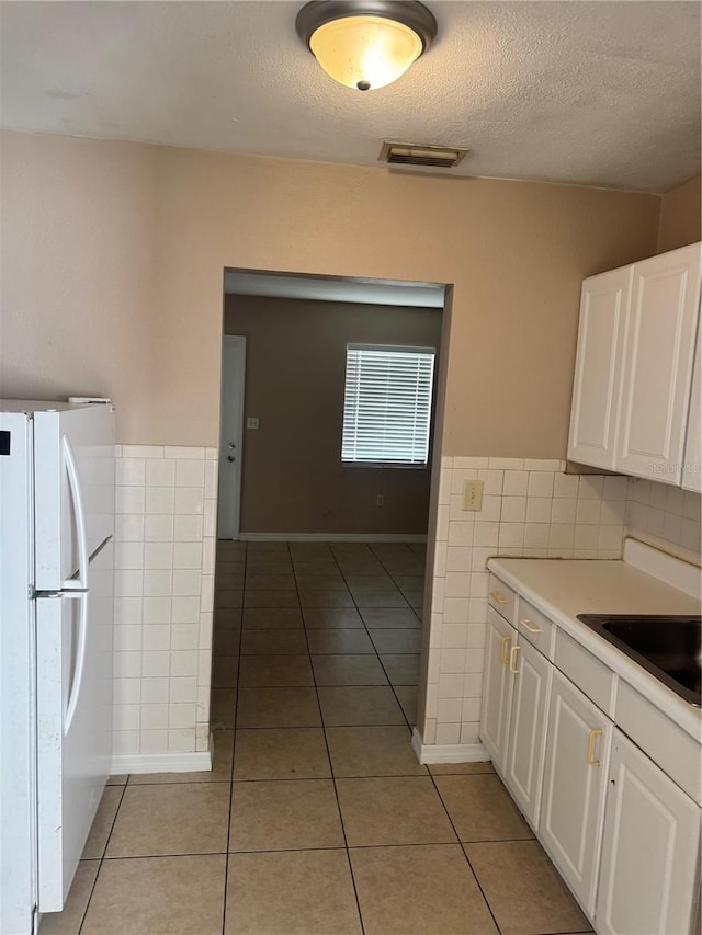 kitchen with light tile patterned floors, white cabinetry, tile walls, white refrigerator, and a textured ceiling