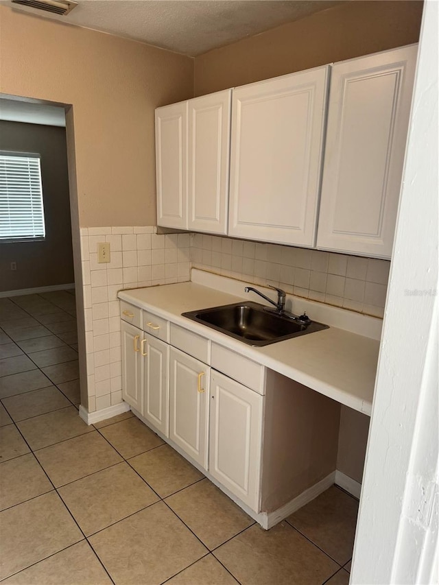 kitchen with tile walls, sink, light tile patterned floors, and white cabinets