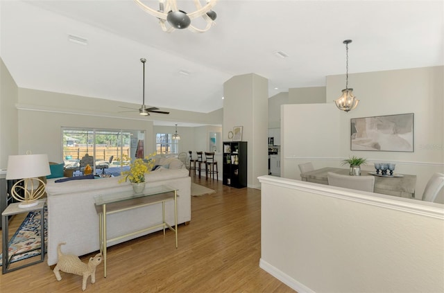 living room featuring ceiling fan with notable chandelier, light wood-type flooring, and vaulted ceiling