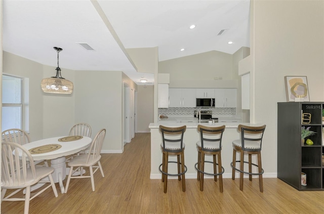 kitchen featuring appliances with stainless steel finishes, decorative light fixtures, white cabinetry, and a breakfast bar