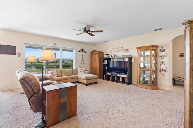 living area featuring carpet floors, arched walkways, visible vents, a ceiling fan, and a textured ceiling