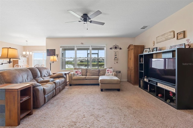 living area featuring a textured ceiling, ceiling fan with notable chandelier, carpet, and visible vents
